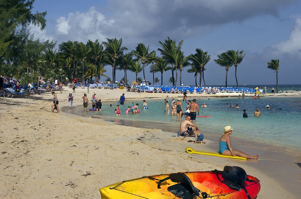 A white sand beach with palm trees, kayaks and clear blue water on CocoCay in the Bahamas