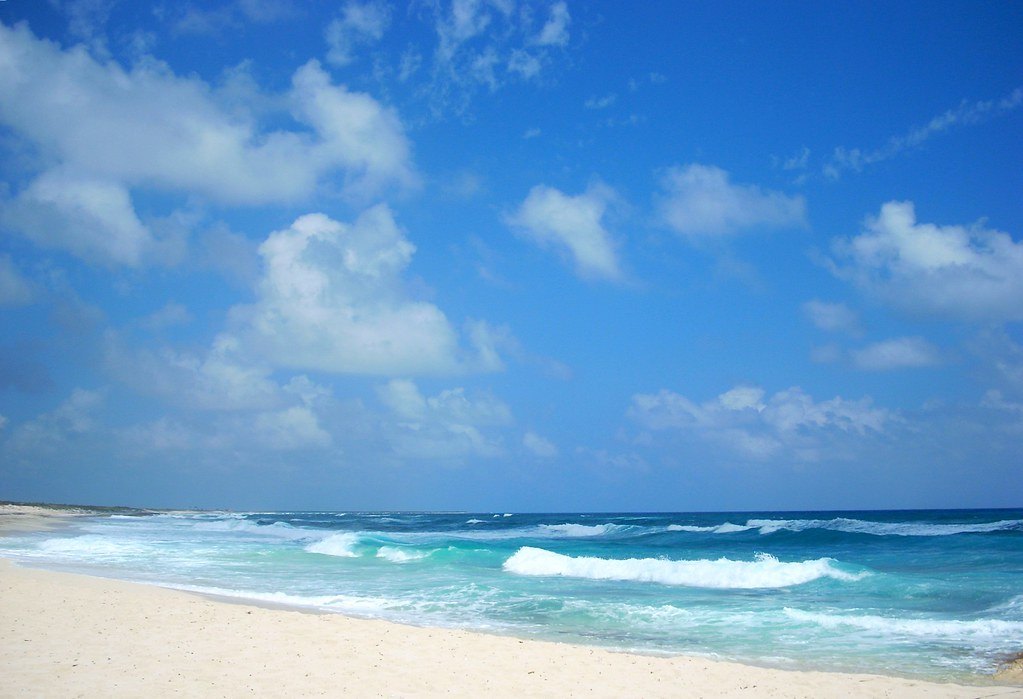 Waves rolling onto a sandy beach in Cozumel, Mexico, under a blue sky