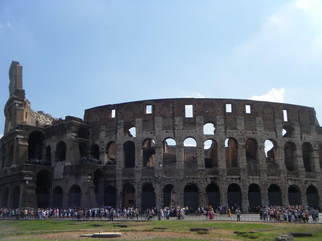 The Colosseum in Rome under a blue sky, with visitors in front