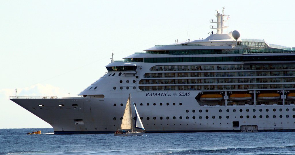 Radiance of the Seas at sea, with a small sailboat passing in front